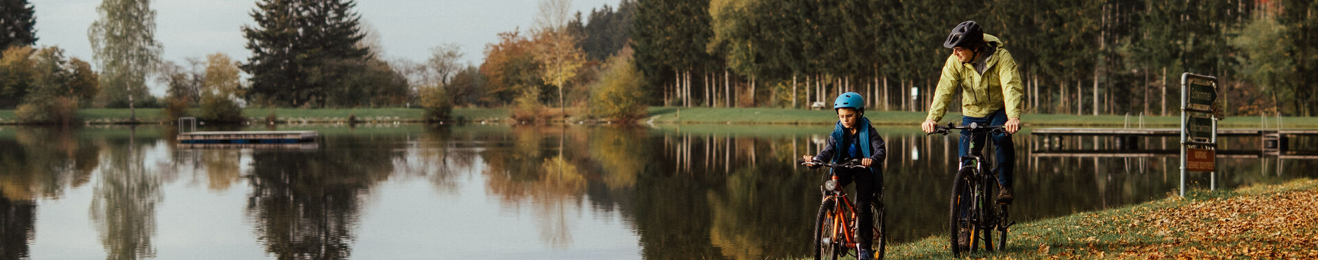 Vater und Sohn fahren mit Rad an Badesee-Ufer; herbstliche Stimmung;